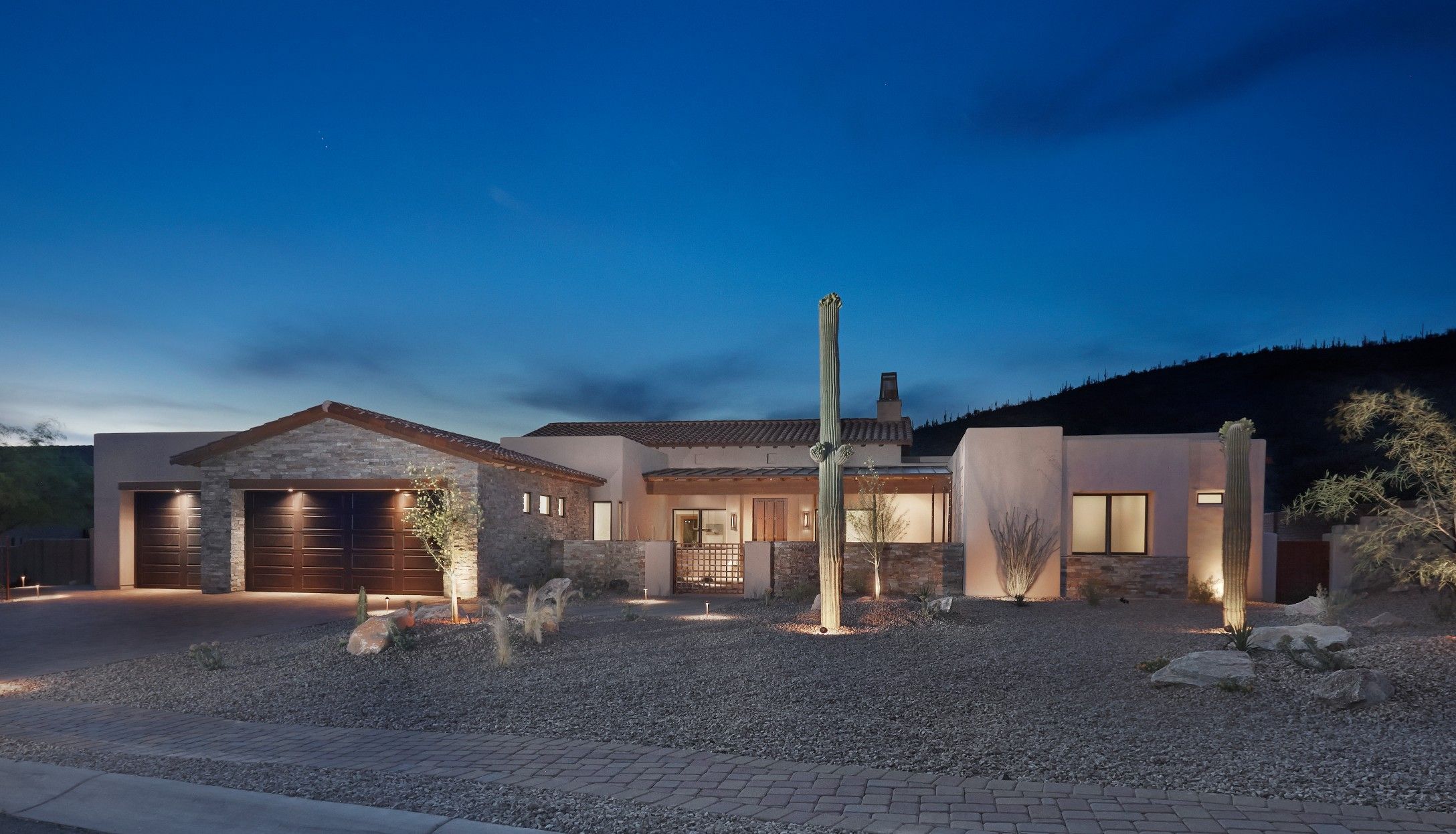 Front elevation at dusk with a lit three-car garage, saguaro and mountain silhouette