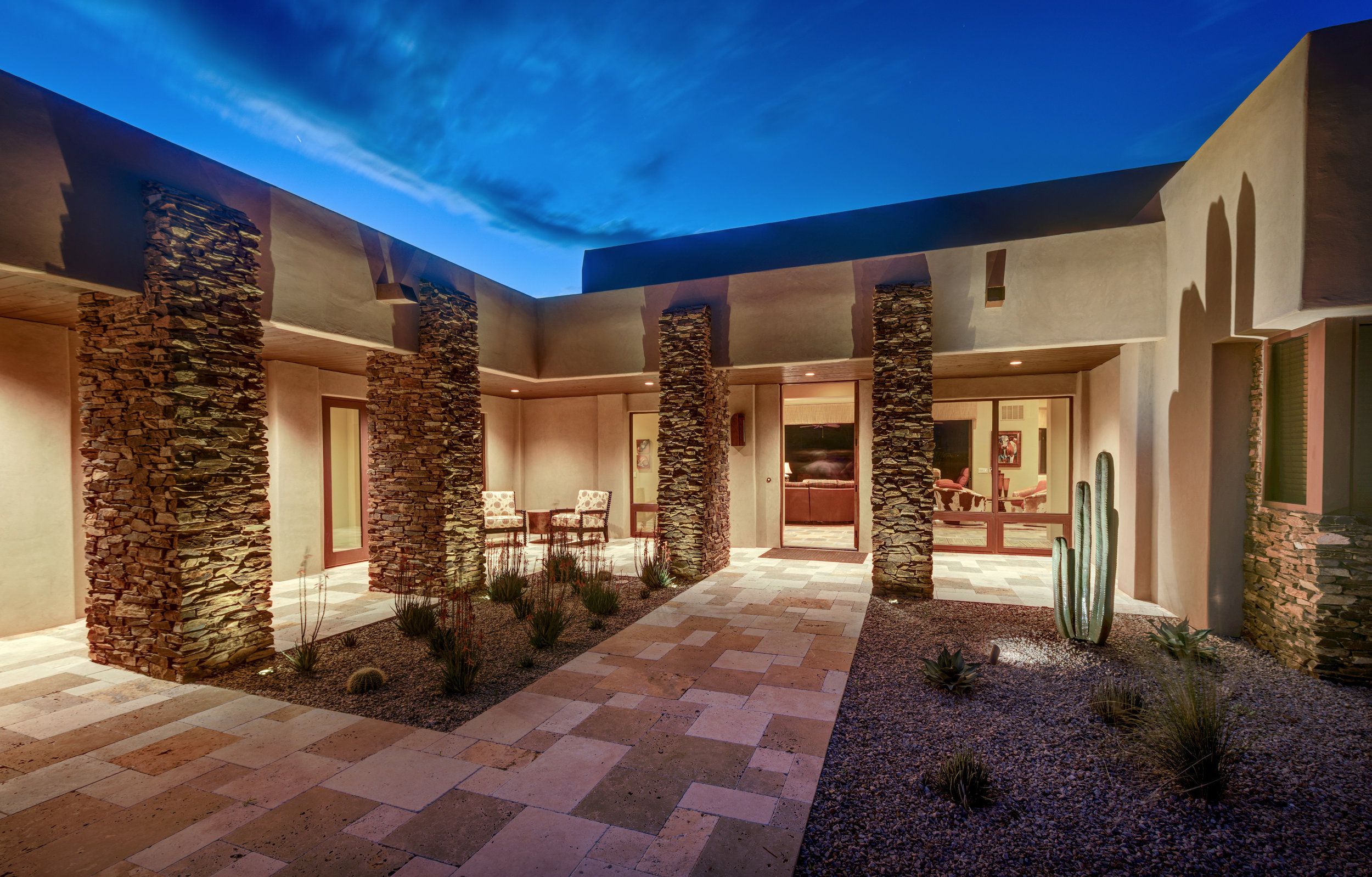 Entry courtyard at dusk with stone columns, a saguaro and paver paving