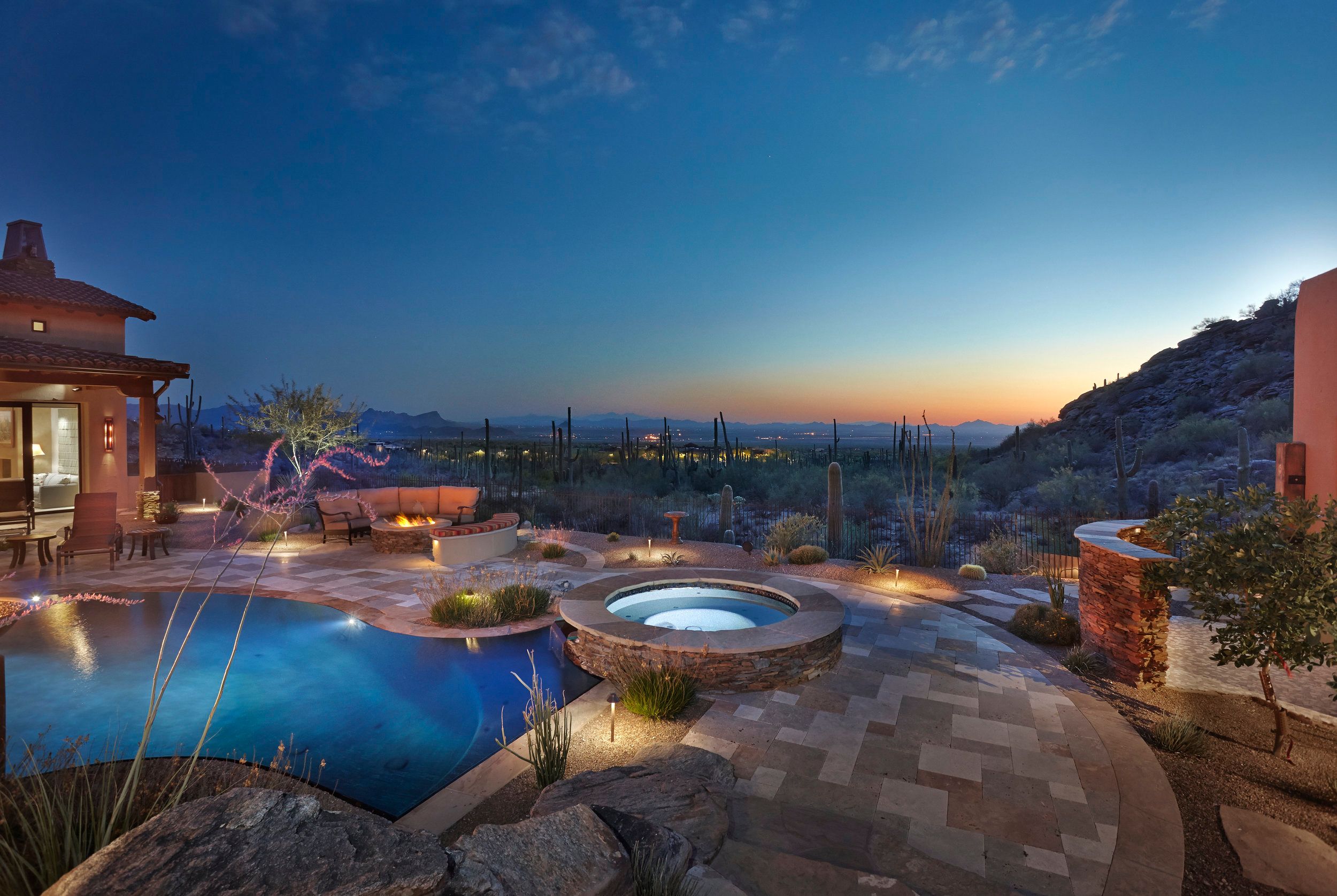 Pool and spa lit at sunset with the desert valley and mountains beyond