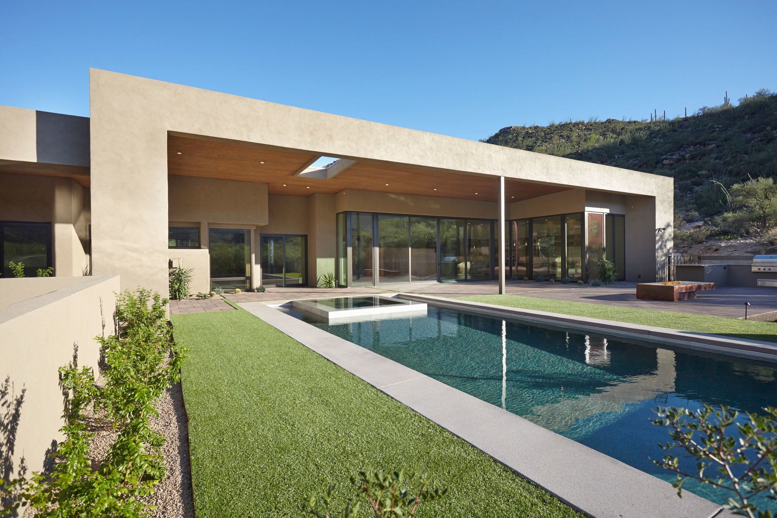 Rear elevation with a deep overhang, lap pool and lawn against the desert hillside