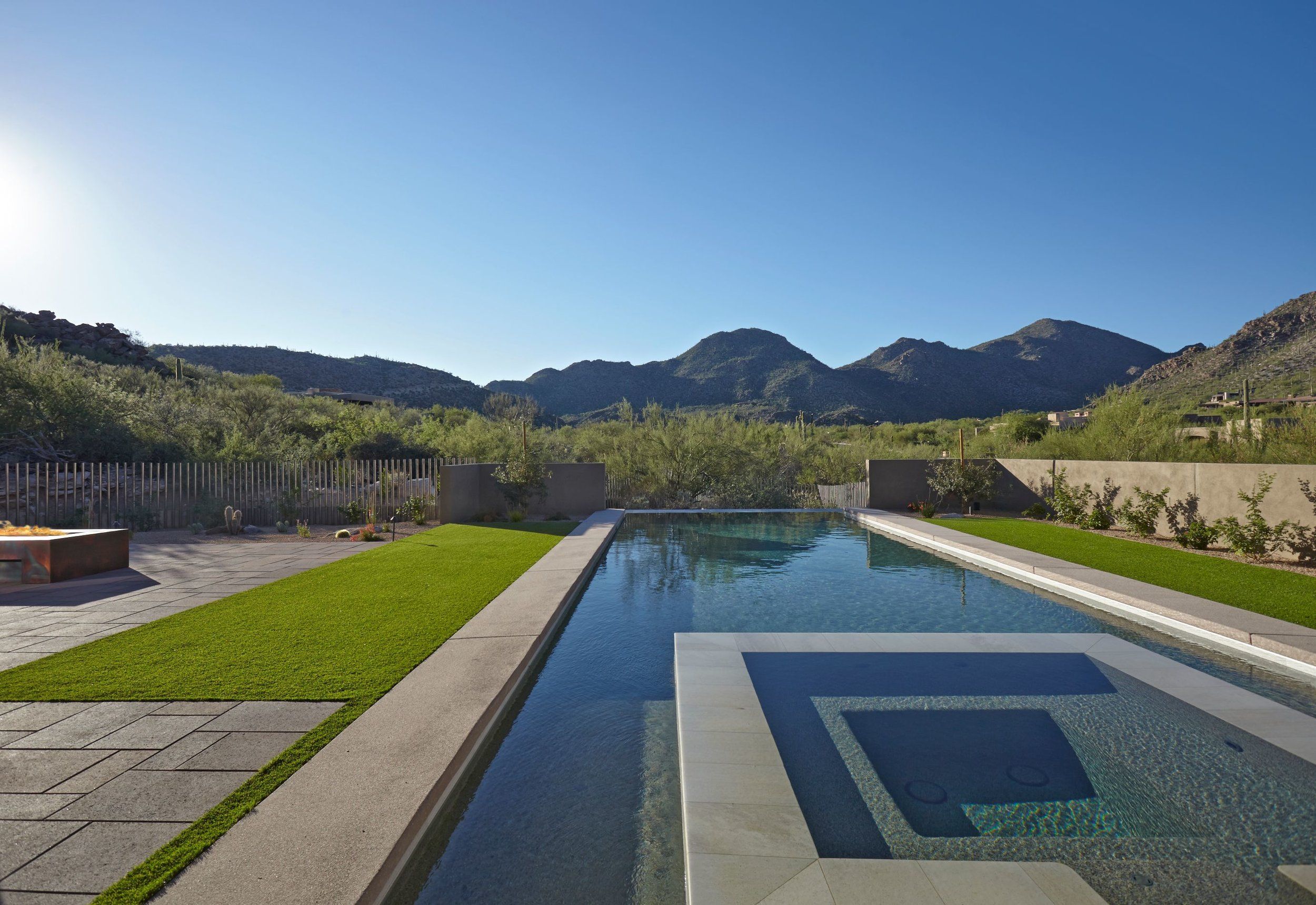 Lap pool and square spa bordered by lawn with mountains on the horizon