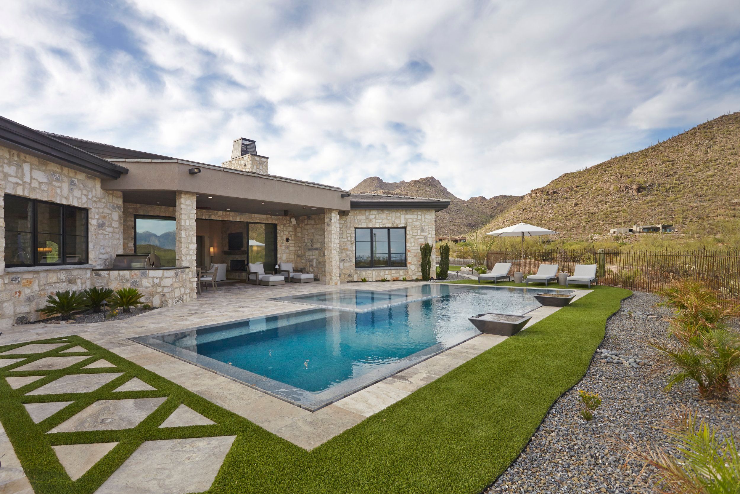 Rear elevation with a negative-edge pool, lawn and stone facade against a desert hillside