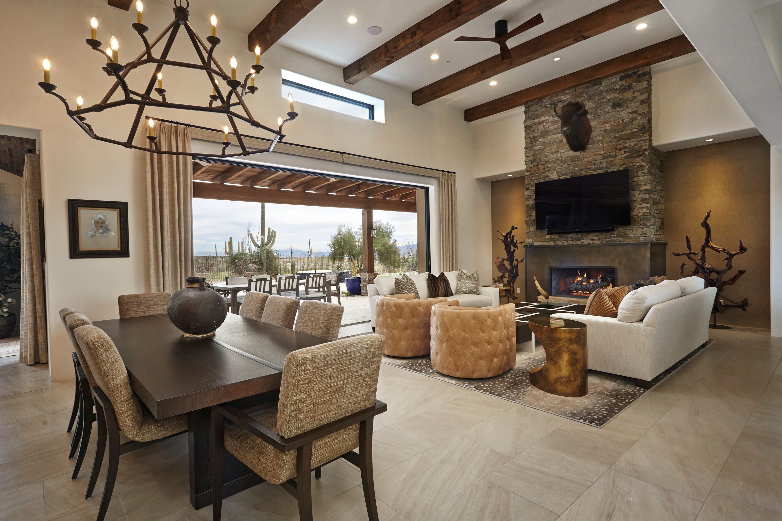 Great room with an iron chandelier, stone fireplace and pocketing glass wall onto the desert
