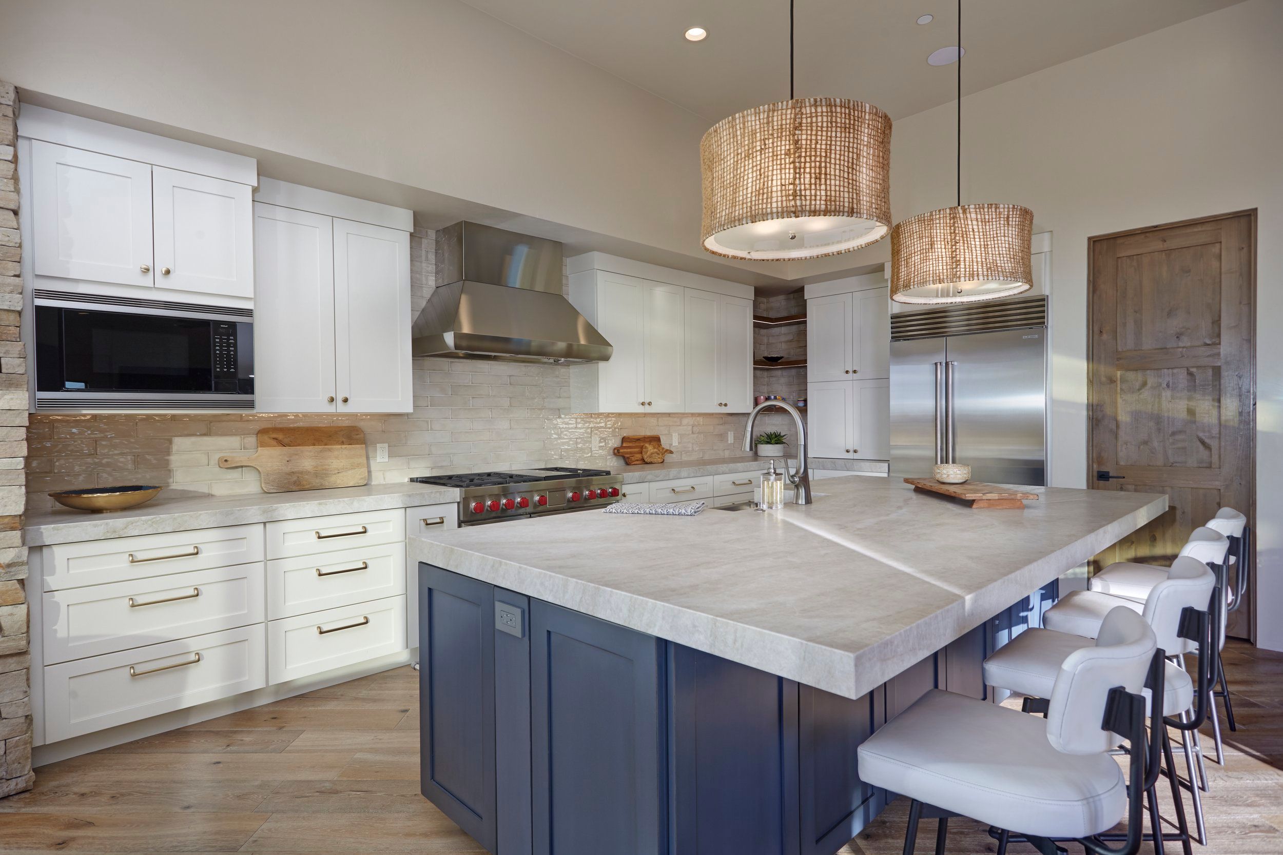 White kitchen with a navy island, marble counters and woven drum pendants