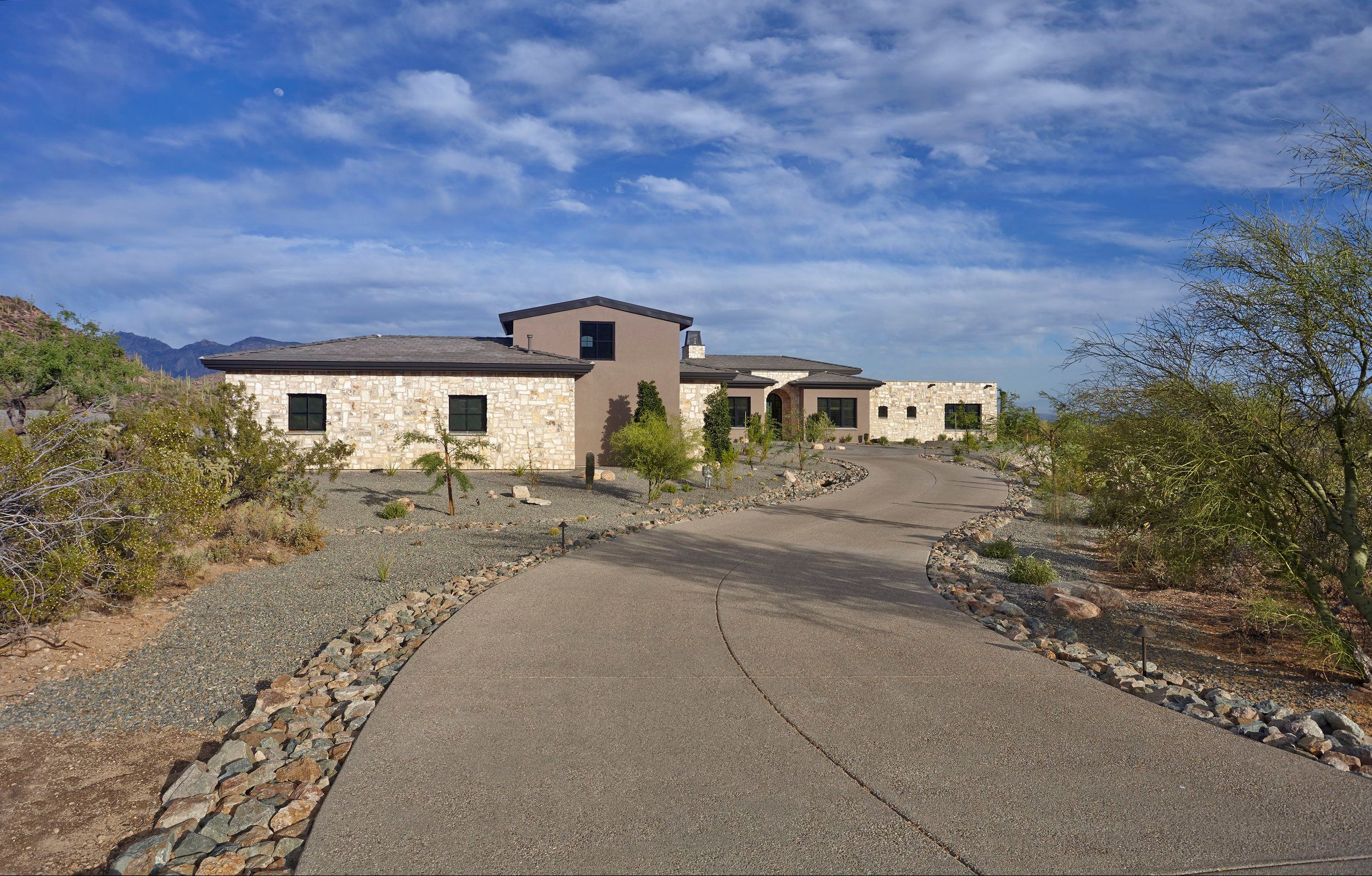 Approach drive curving toward the stone and stucco home set in the desert