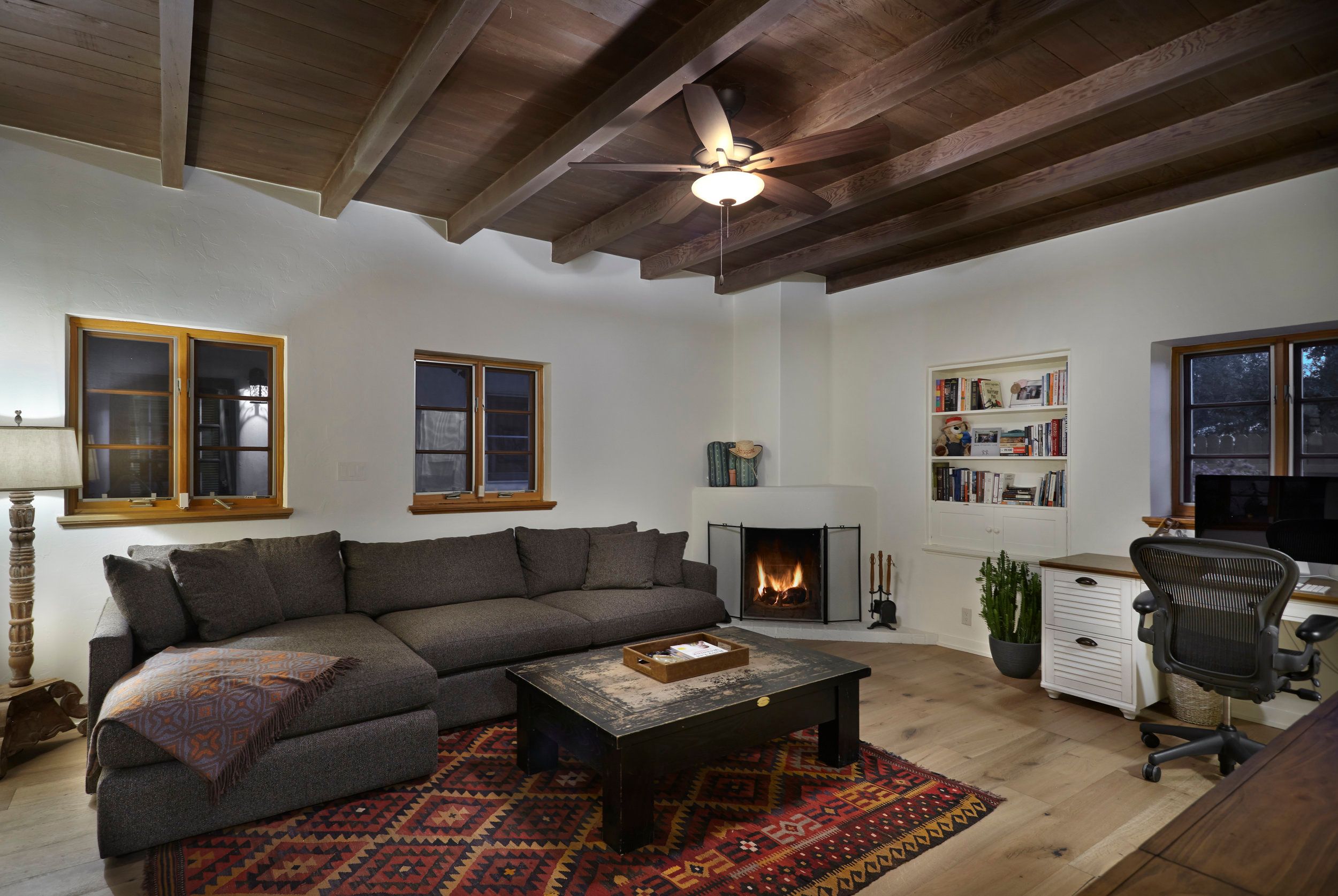 Family room with dark beamed ceiling, corner fireplace and a kilim rug