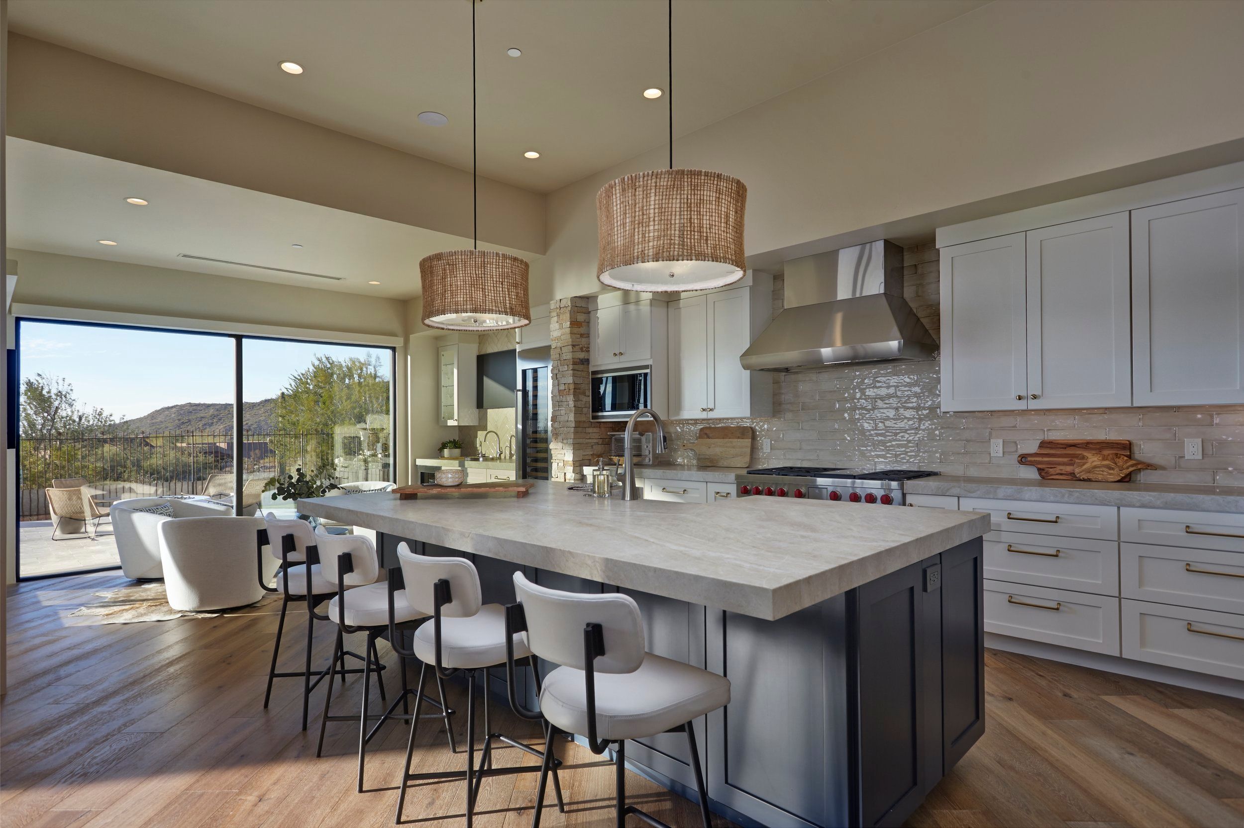 White kitchen with a waterfall marble island, woven pendant lights and sliding doors to a mountain view