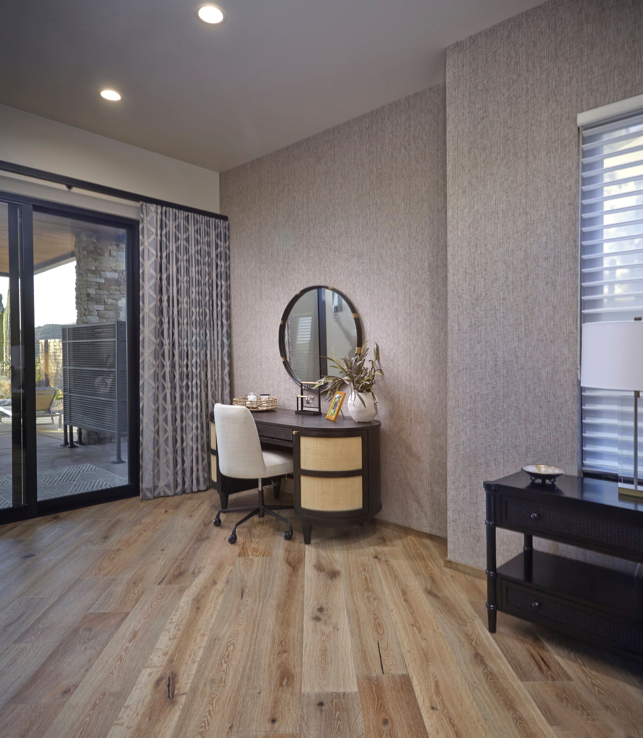 Bedroom corner with a round mirror, vanity desk and sliding door to the patio