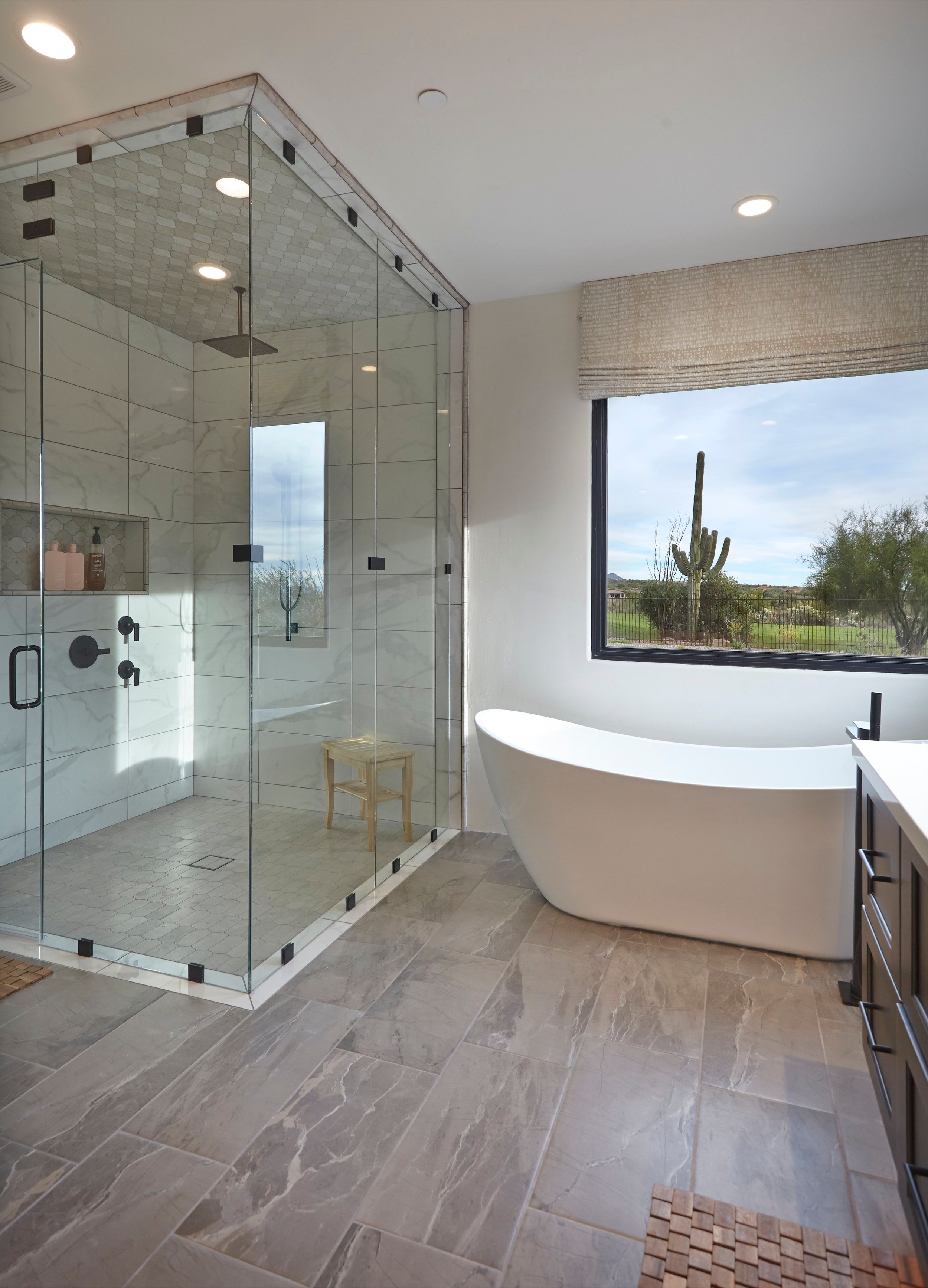 Glass shower enclosure and freestanding tub with a saguaro framed in the window