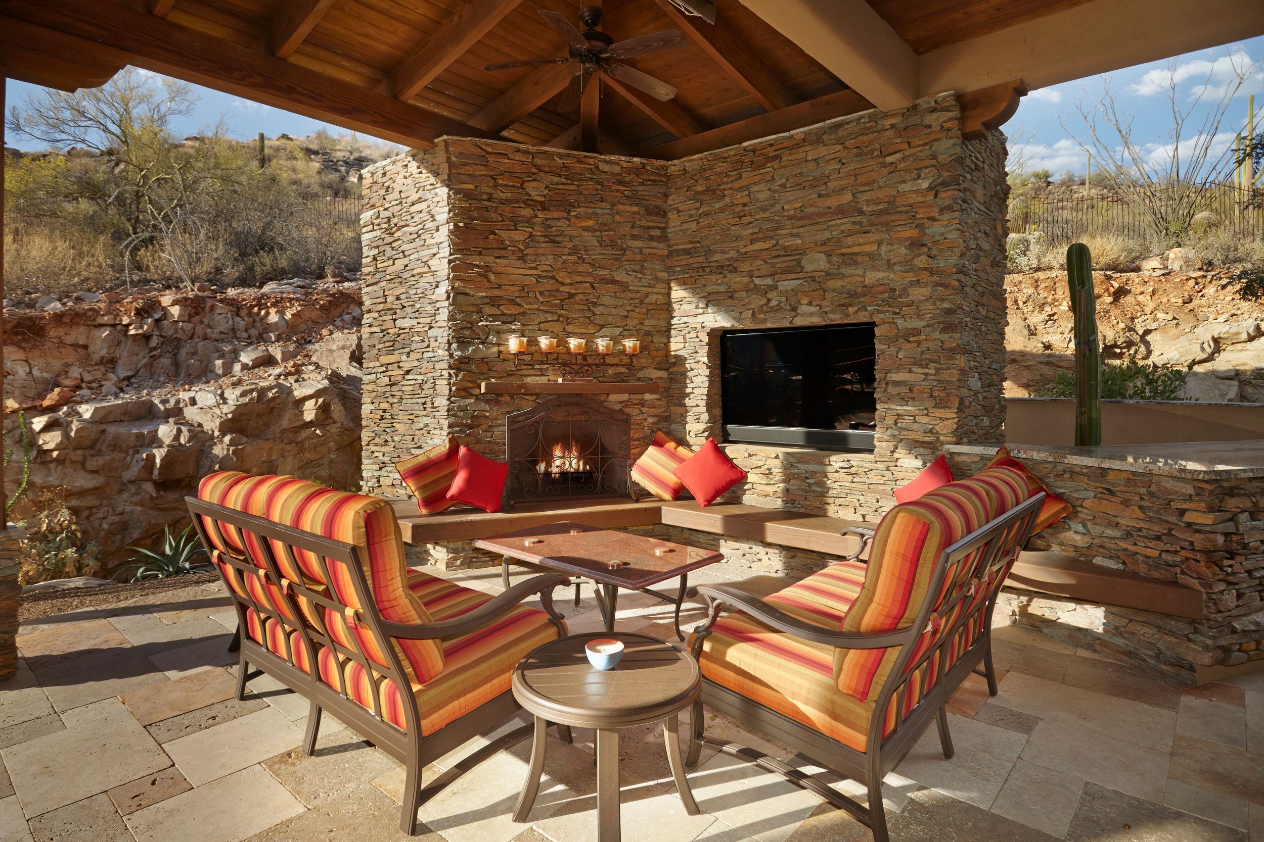 Covered patio with a stacked-stone fireplace, television and striped lounge chairs