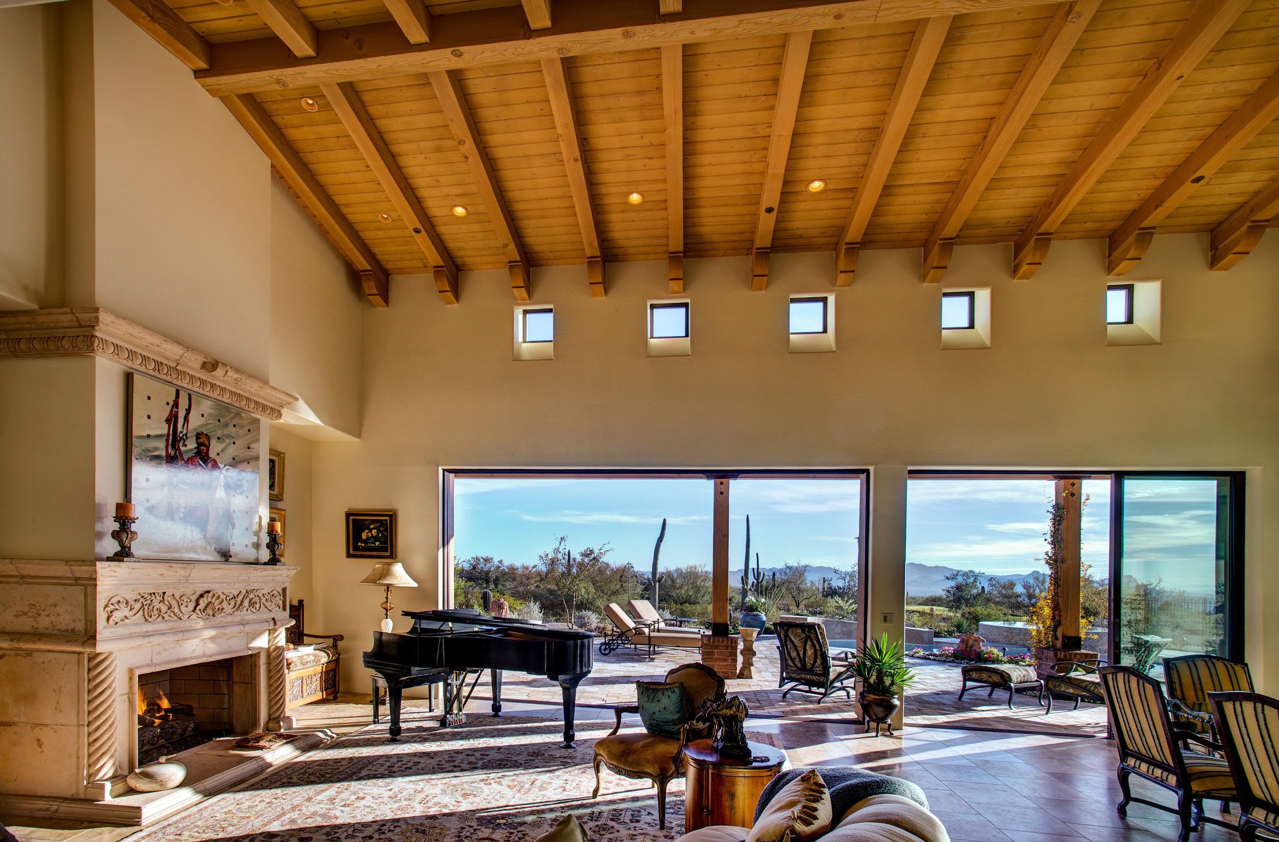 Great room with a grand piano and carved stone mantel beneath a vaulted wood-plank ceiling
