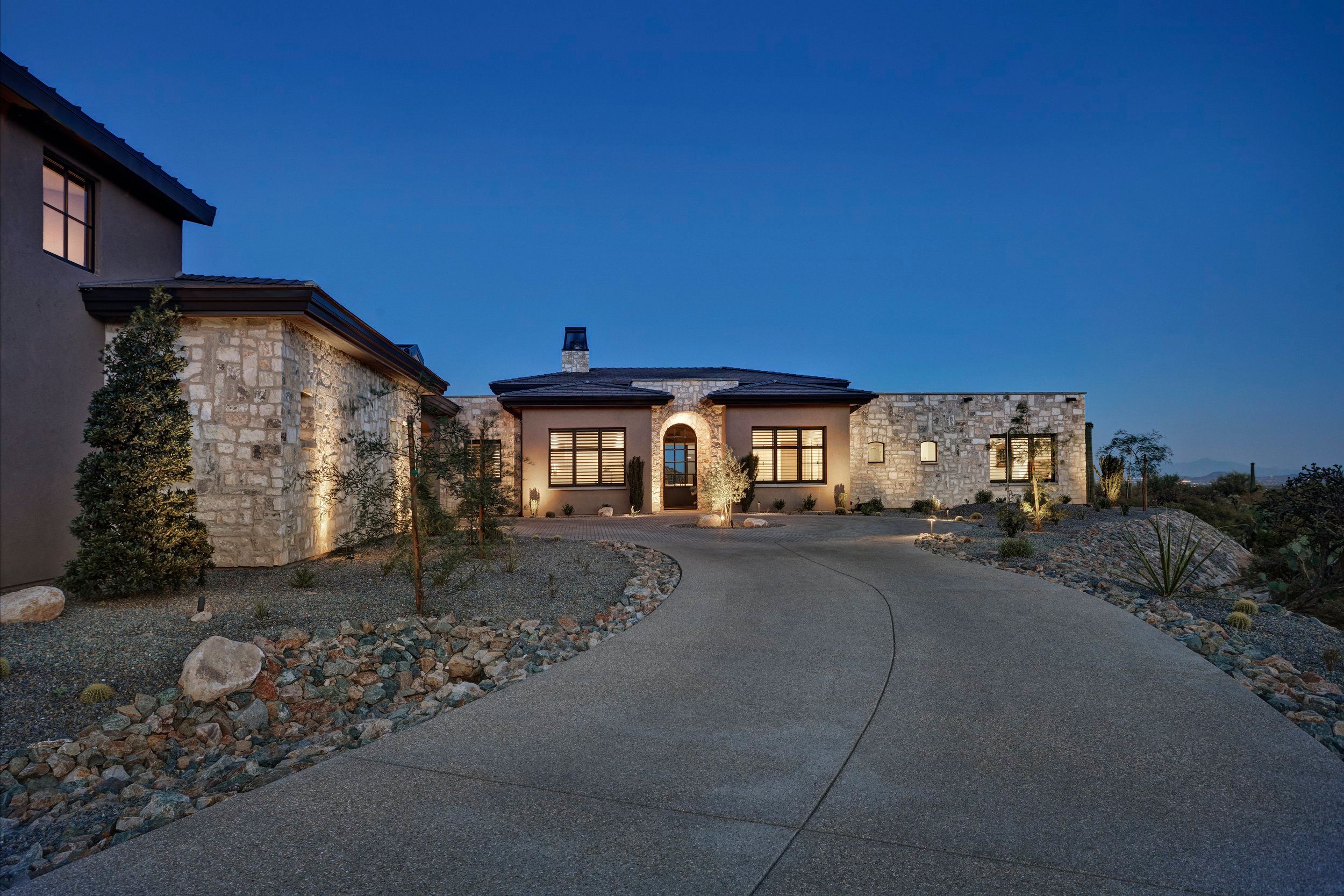 Lit stone facade seen from the curving approach drive at twilight
