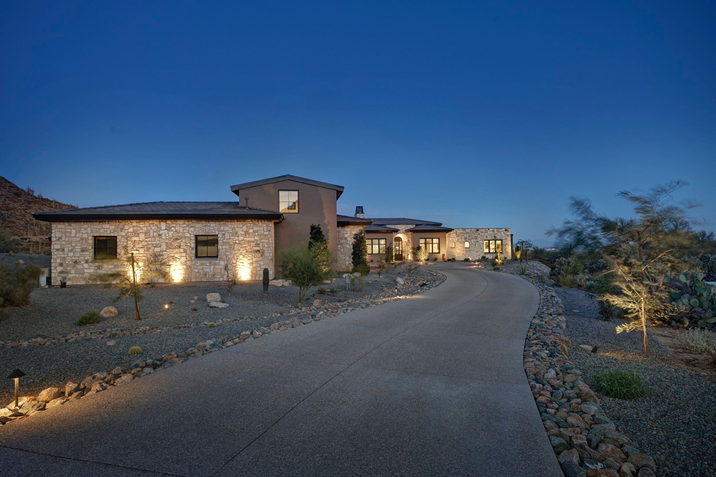 Low stone elevation glowing at twilight beside the desert driveway