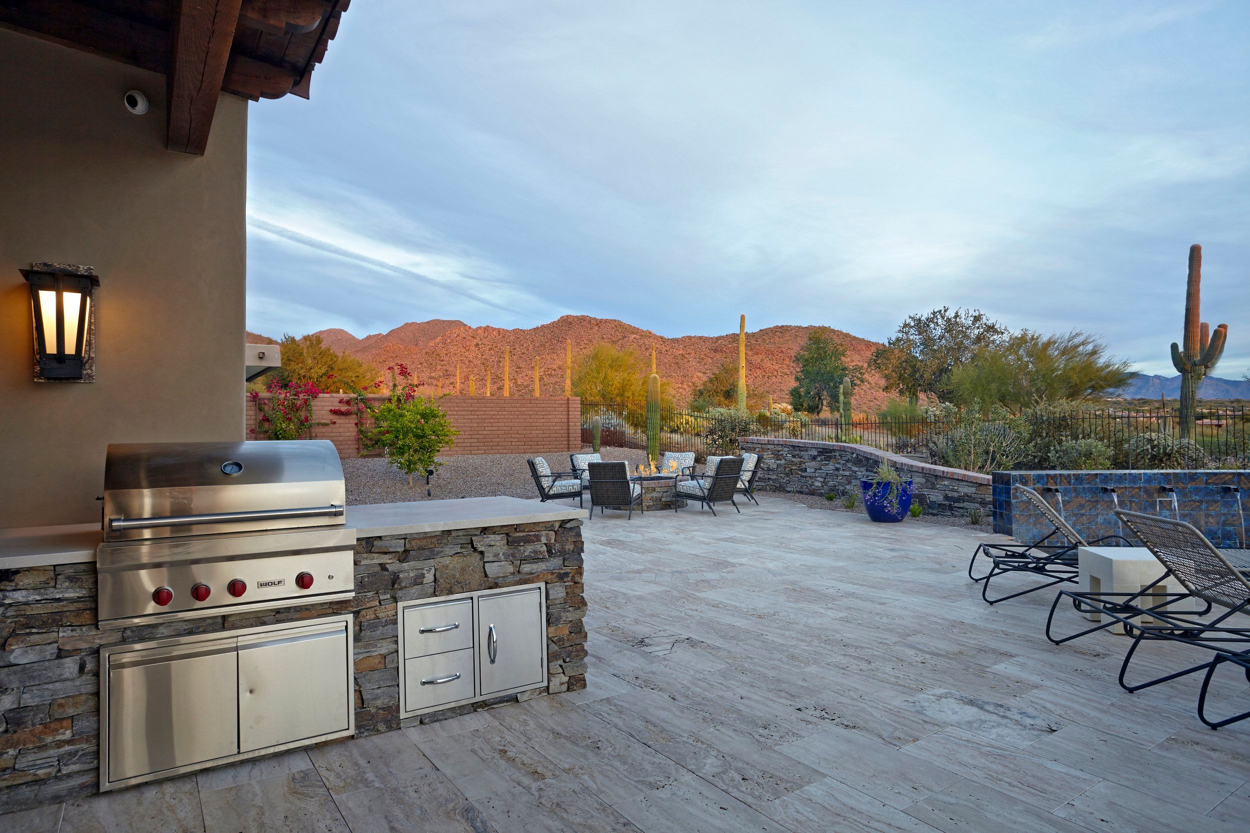 Outdoor kitchen with a built-in grill on a travertine deck, mountains catching sunset light