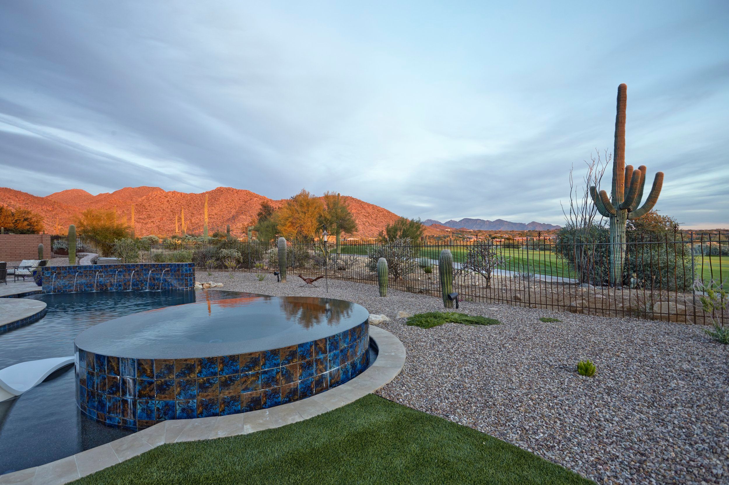 Circular tiled spa beside the pool with the Tortolita Mountains glowing at sunset