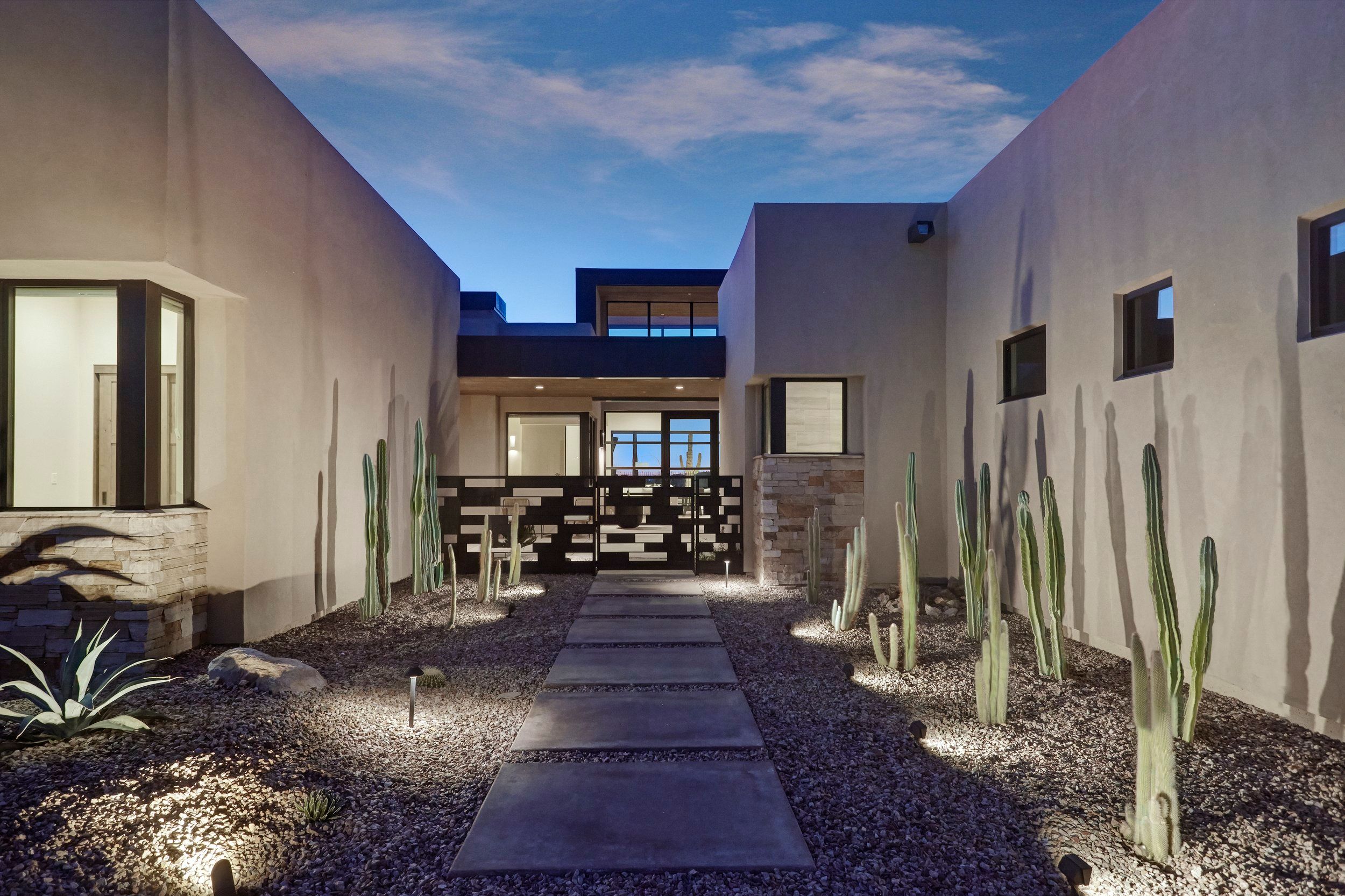 Entry courtyard at twilight with a stone path, organ pipe cactus and uplighting
