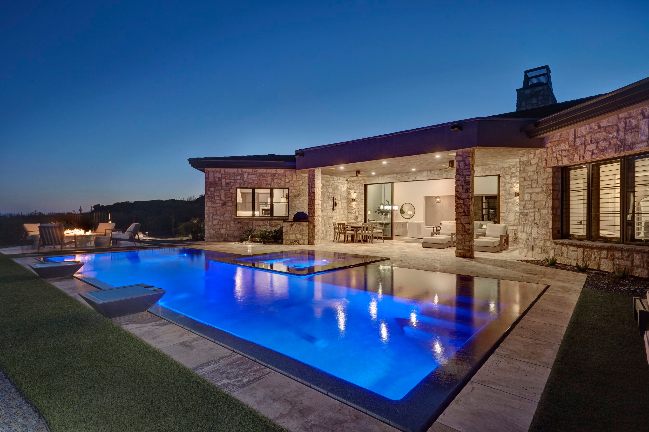 Lit pool at dusk running alongside the covered patio and great room