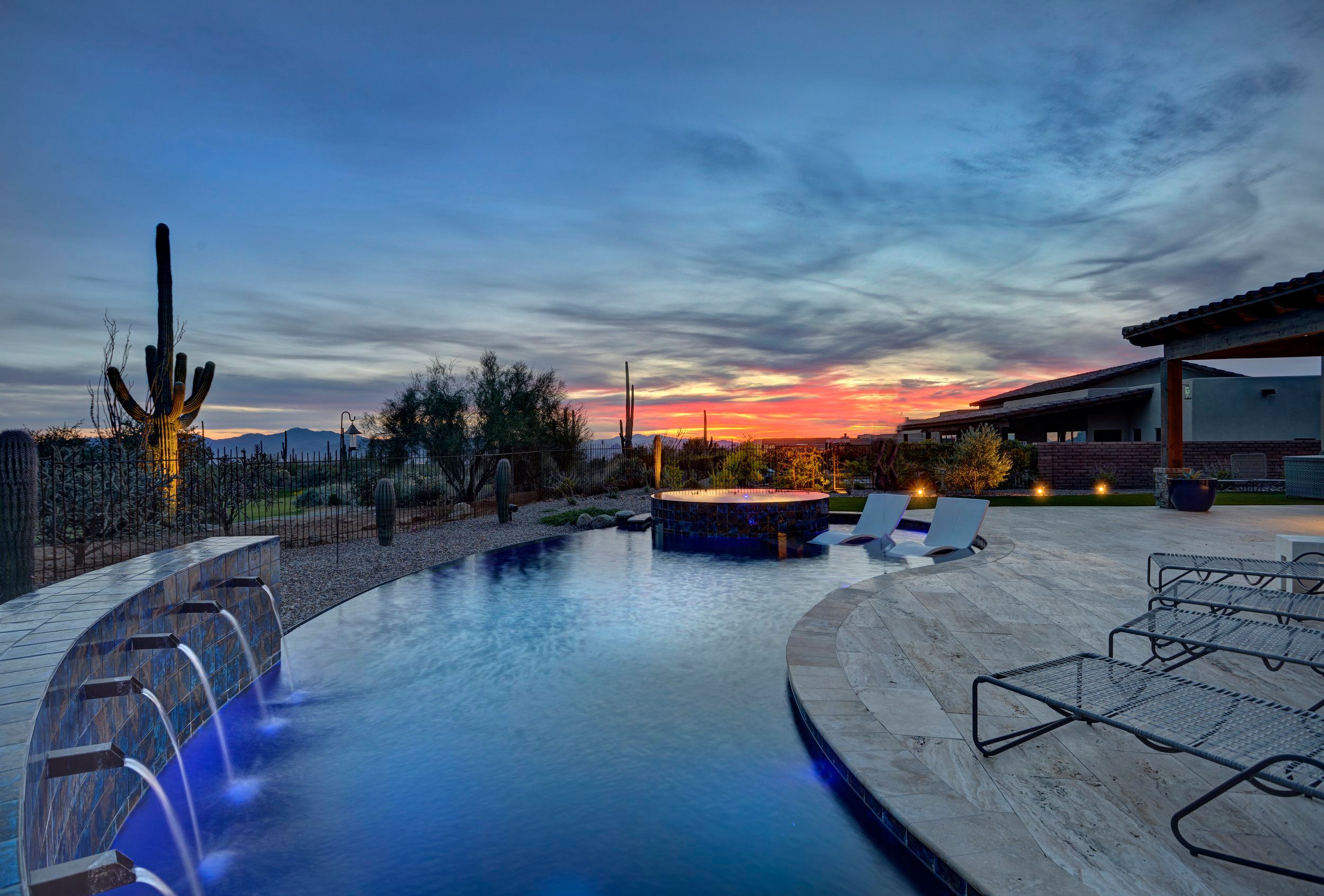 Pool with a water feature at sunset, saguaros silhouetted against an orange horizon