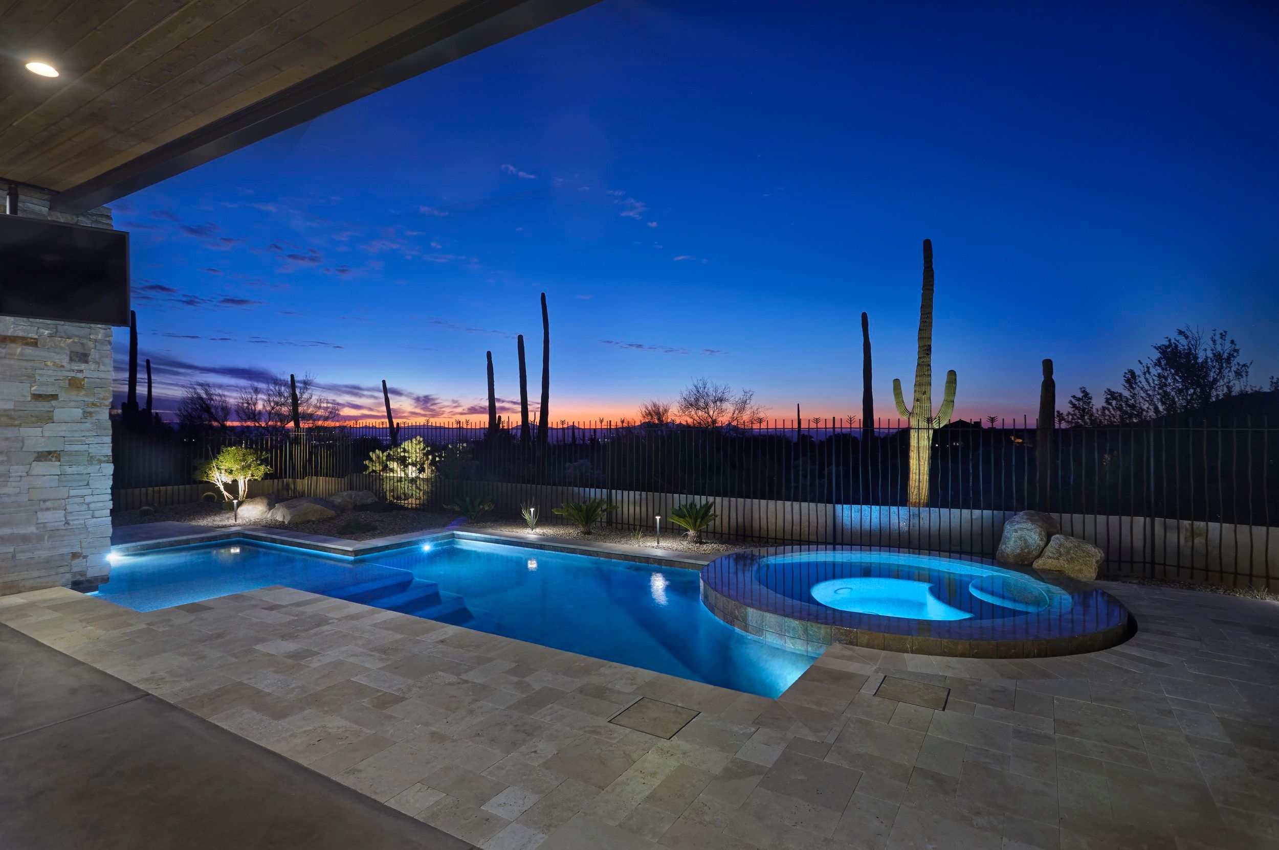 Pool and spa lit at dusk with saguaros against an orange horizon