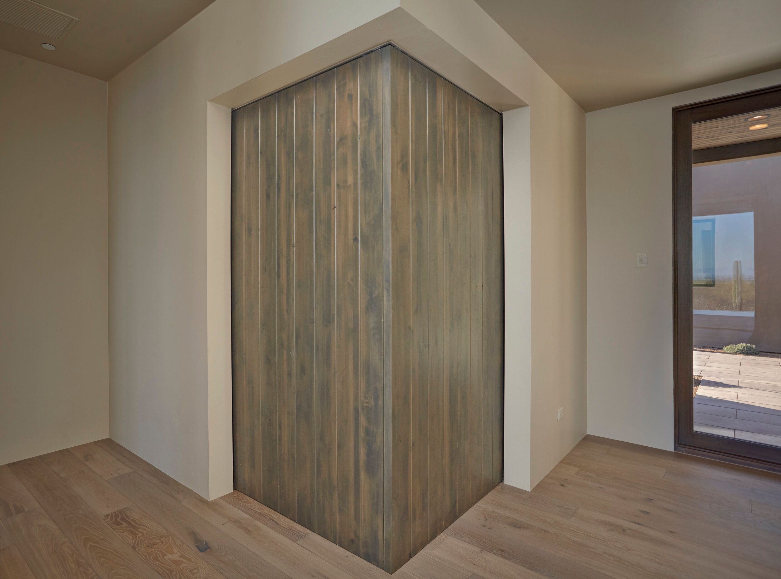 Corner detail of a timber-clad wall against white plaster and oak flooring
