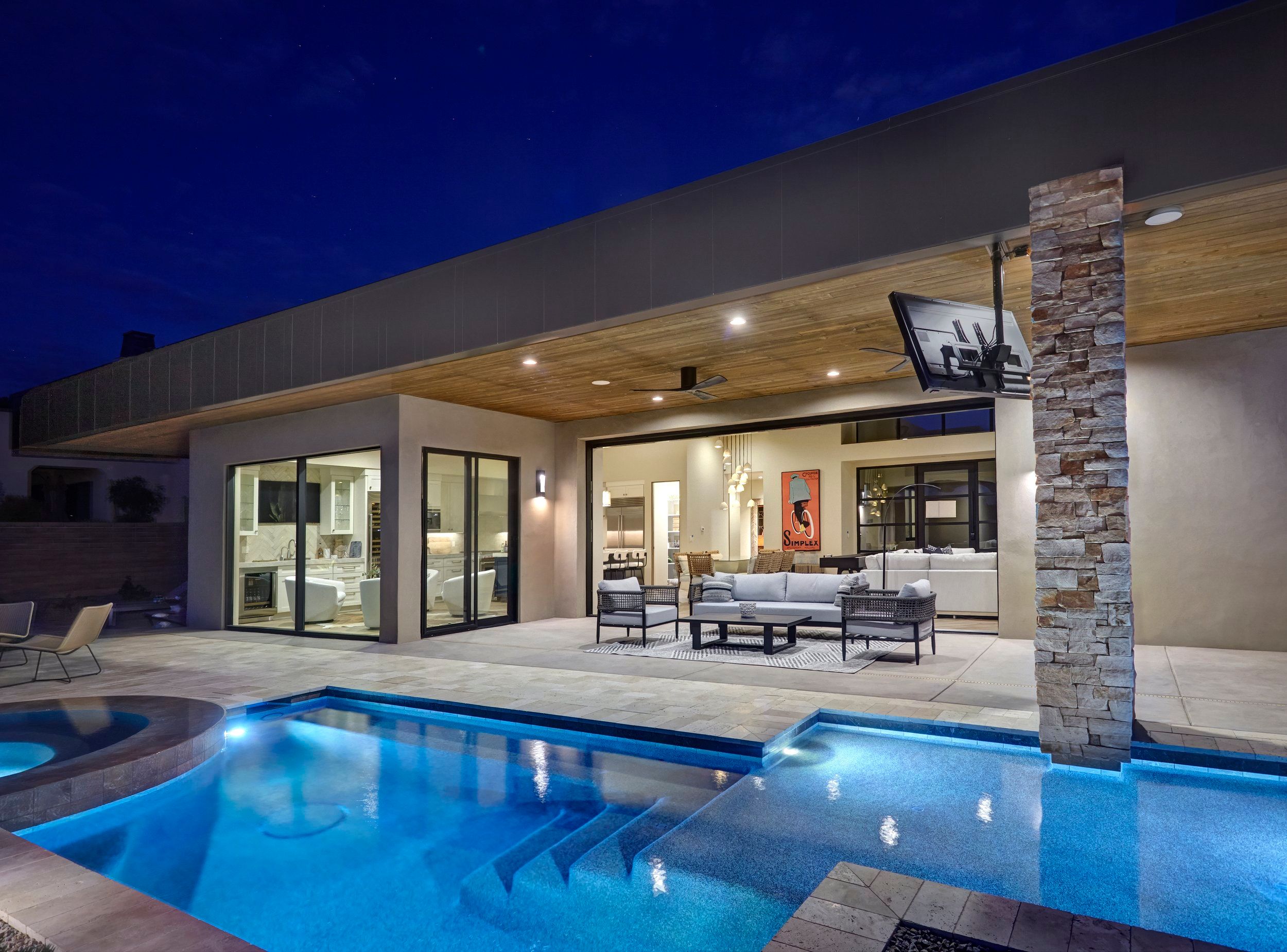 Covered patio and lit pool at night with the great room glowing beyond