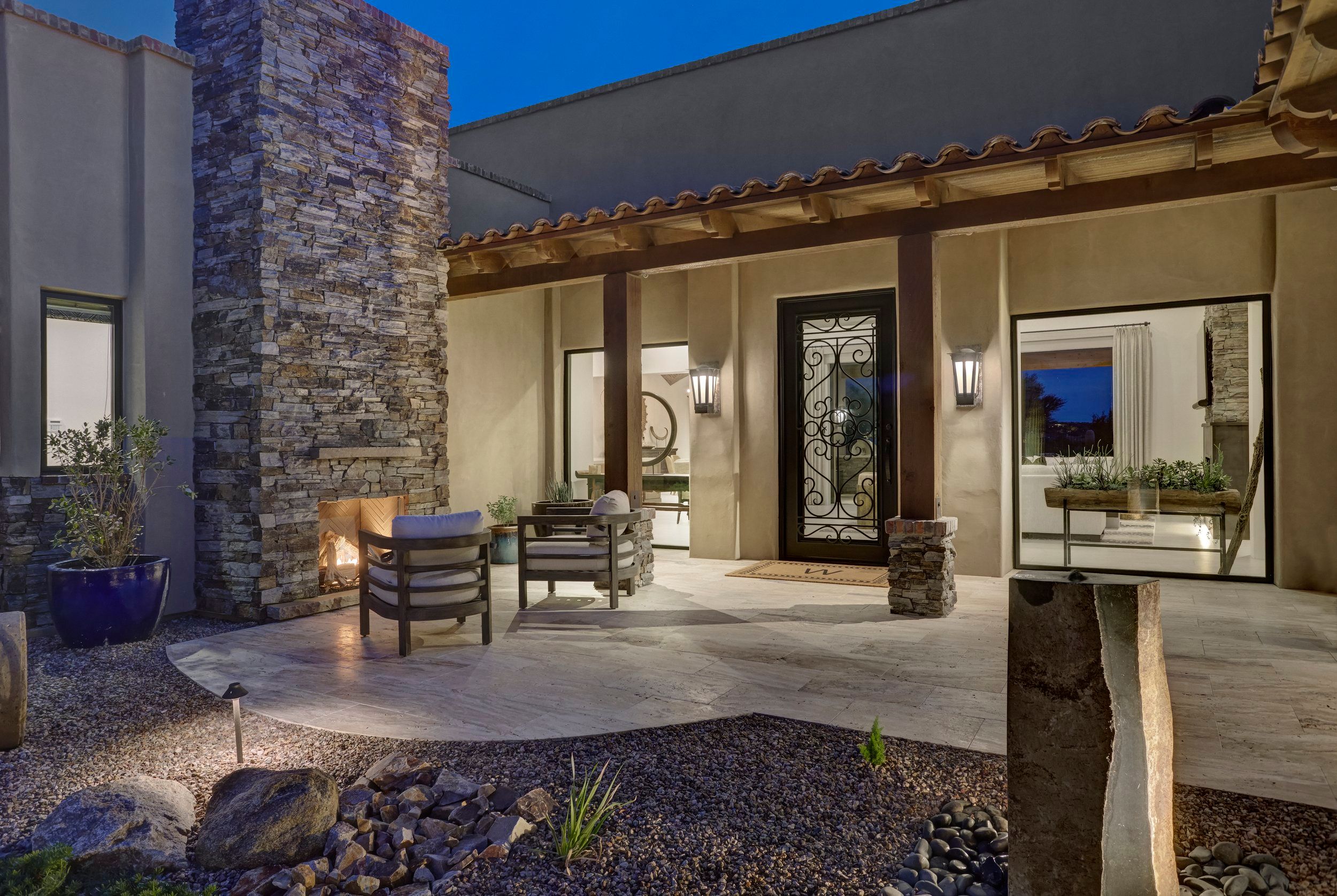 Entry courtyard with a stone chimney, patio seating and a wrought-iron front door
