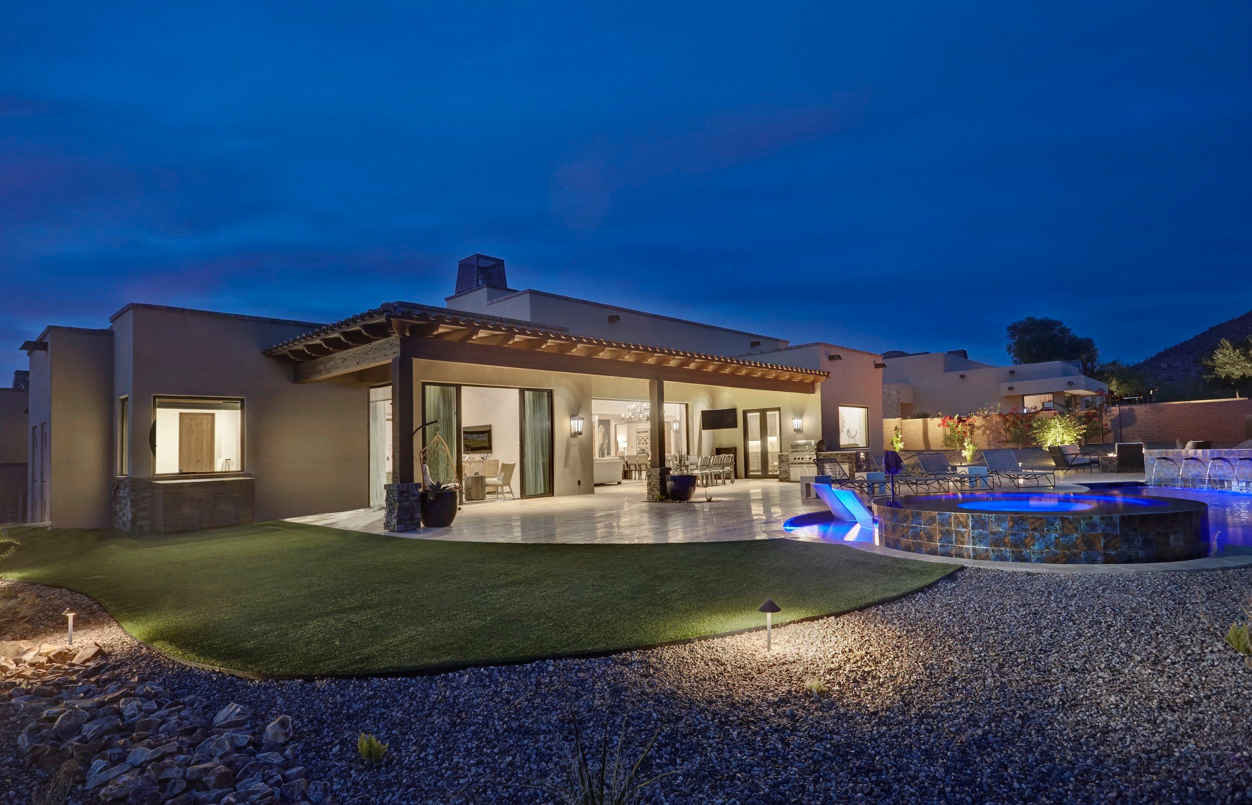 Rear elevation at dusk with a lawn, covered patio and lit pool and spa