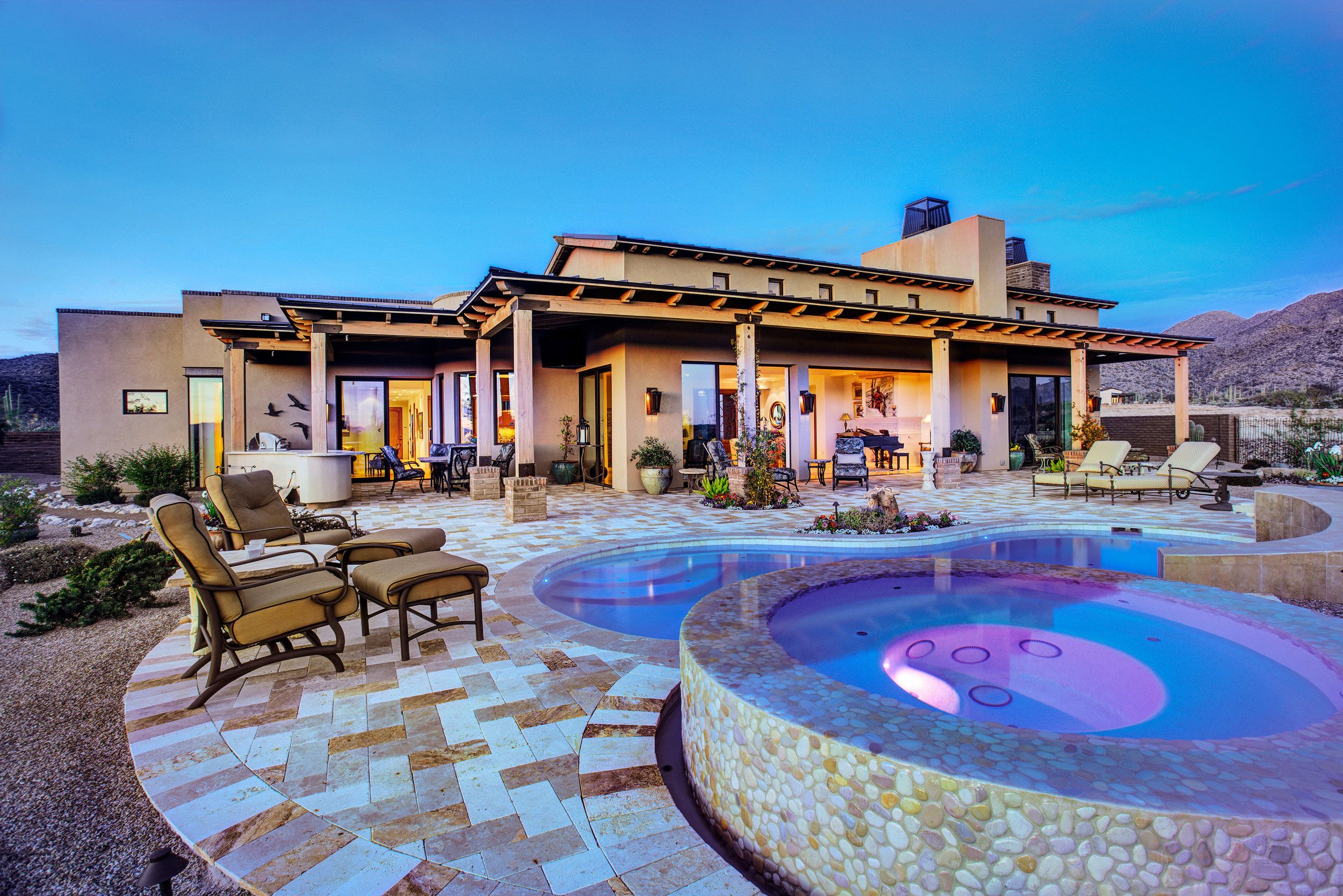 Lit spa and pool at dusk with the house glowing behind the covered patio