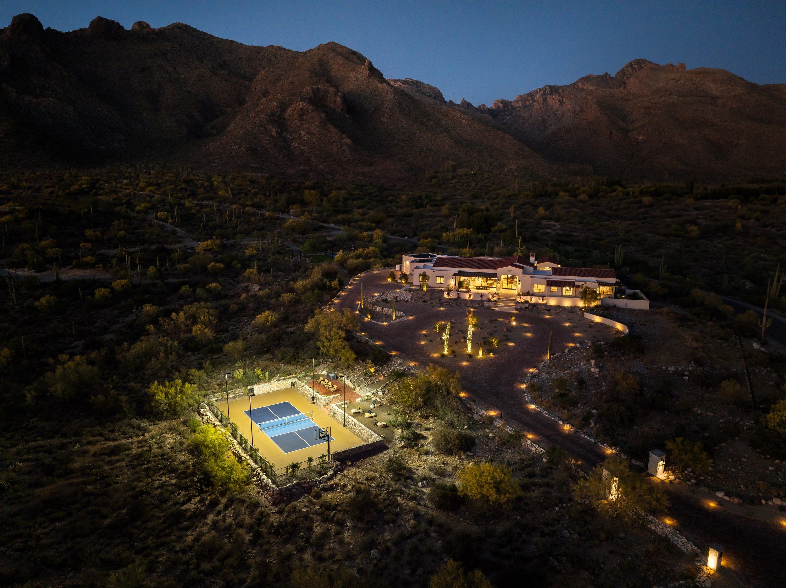 Aerial at dusk of the lit house and sport court in the desert